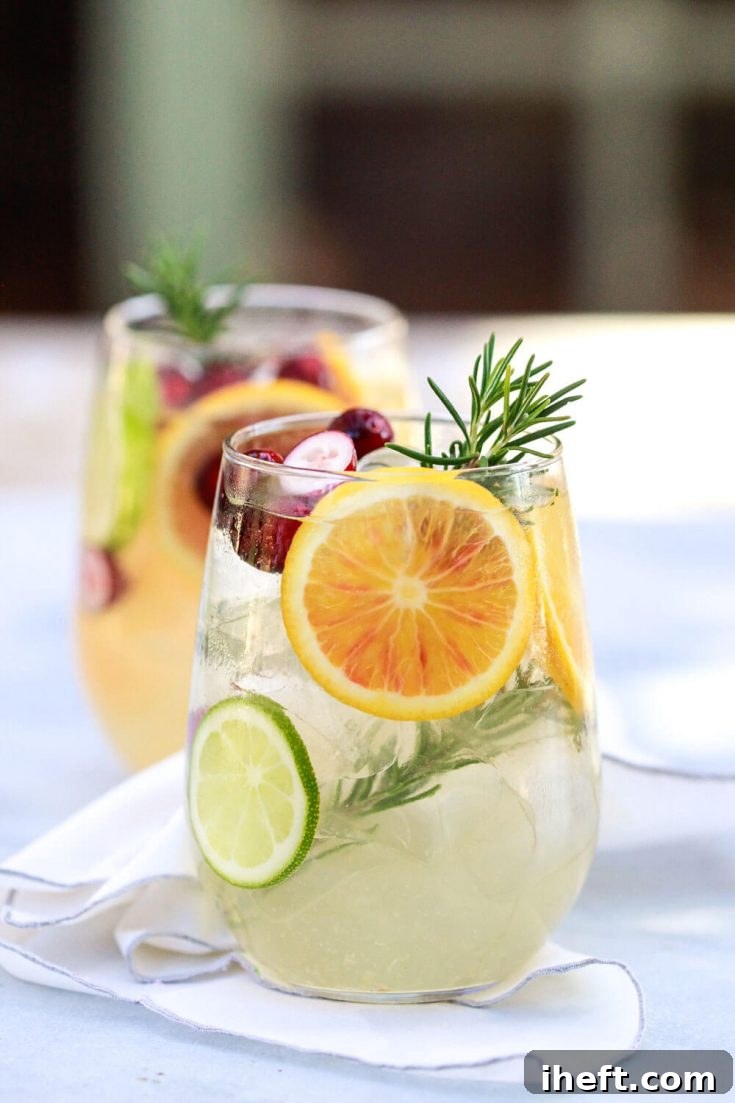 Pinnable image for White Sangria recipe, featuring a beautiful glass with citrus, cranberries, and rosemary.