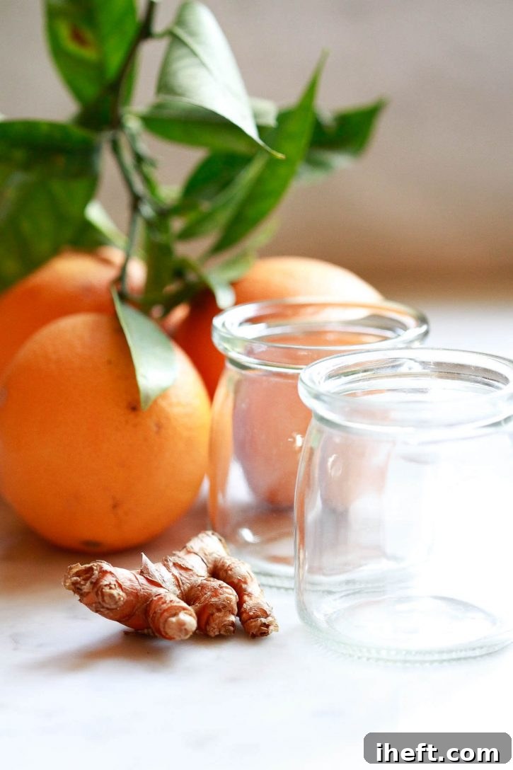 A vibrant, close-up shot of fresh turmeric root and oranges, the primary ingredients for homemade wellness shots, beautifully arranged on a rustic wooden surface, highlighting their natural goodness.