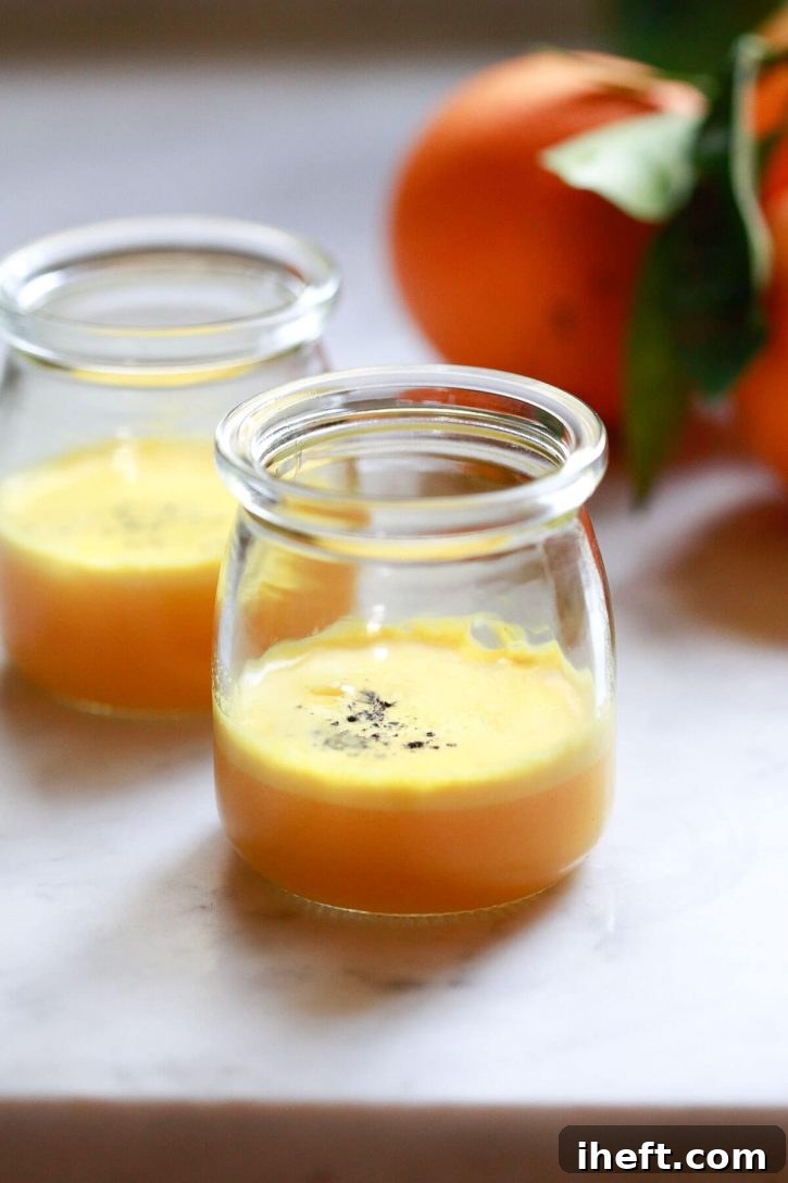 Two small, clear jars containing homemade orange turmeric shots, each generously topped with a sprinkle of freshly ground black pepper. These potent wellness shots are presented as a natural, anti-inflammatory remedy, ready for consumption.