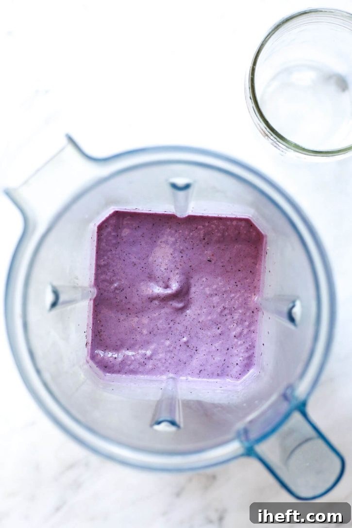 A vibrant purple blueberry banana smoothie, freshly blended and swirling in a Vitamix blender, ready to be poured. This healthy chia seed smoothie promises a delicious and creamy texture.