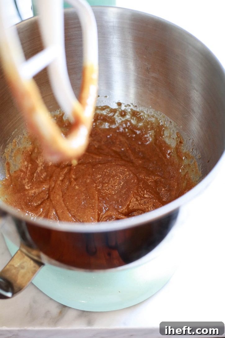The creamy, blended wet ingredients for vegan peanut butter oat cookies swirling in the bowl of a KitchenAid stand mixer, ready for the dry components.