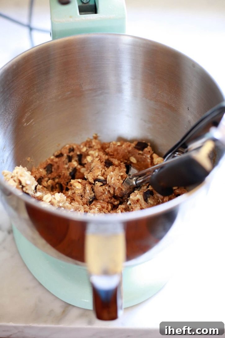 A cookie scoop lifting a perfect portion of vegan cowboy cookie dough from the mixer bowl, showcasing the ideal texture before baking.