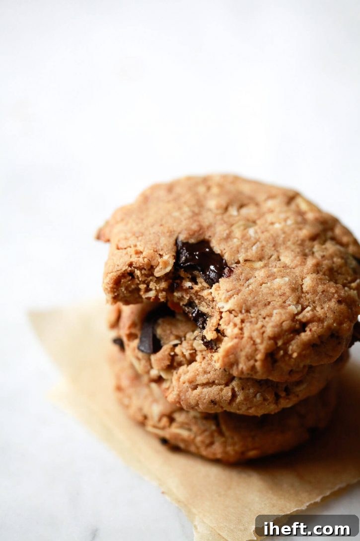 A stack of three freshly baked, golden-brown vegan peanut butter oatmeal cookies, rich with dark chocolate chunks, resting on a cool, smooth marble countertop, ready for a taste test.