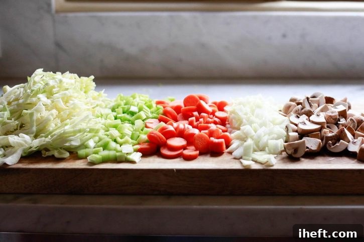 A vibrant array of chopped fresh vegetables including shredded green cabbage, diced celery, sliced carrots, minced onion, and quartered mushrooms, perfectly prepped on a cutting board for a wholesome vegetable cabbage soup.