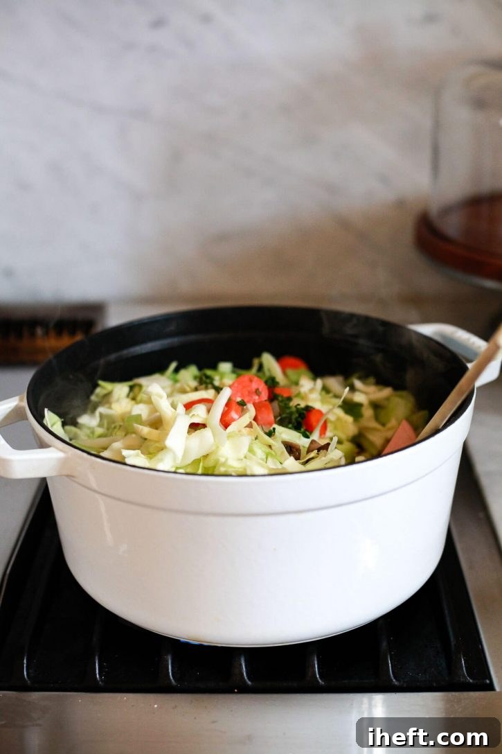 A pristine white Staub pot filled with a colorful medley of sautéed vegetables and shredded green cabbage, ready to simmer into a delicious and healthy weight loss and detox cabbage soup.