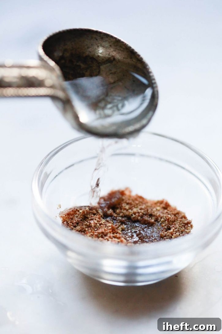 A tablespoon of warm water being carefully poured into a bowl of flax meal, initiating the flax egg creation process.