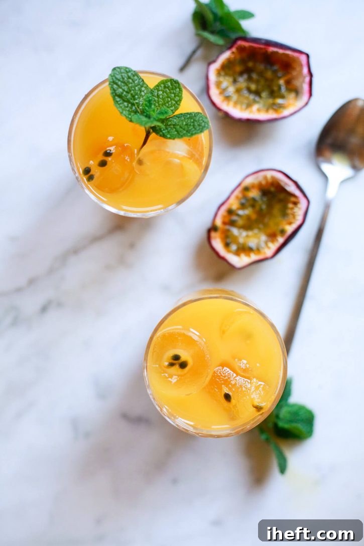 Two glasses filled with vibrant passion fruit juice, garnished with mint. A halved passion fruit sits on a marble countertop in the background.