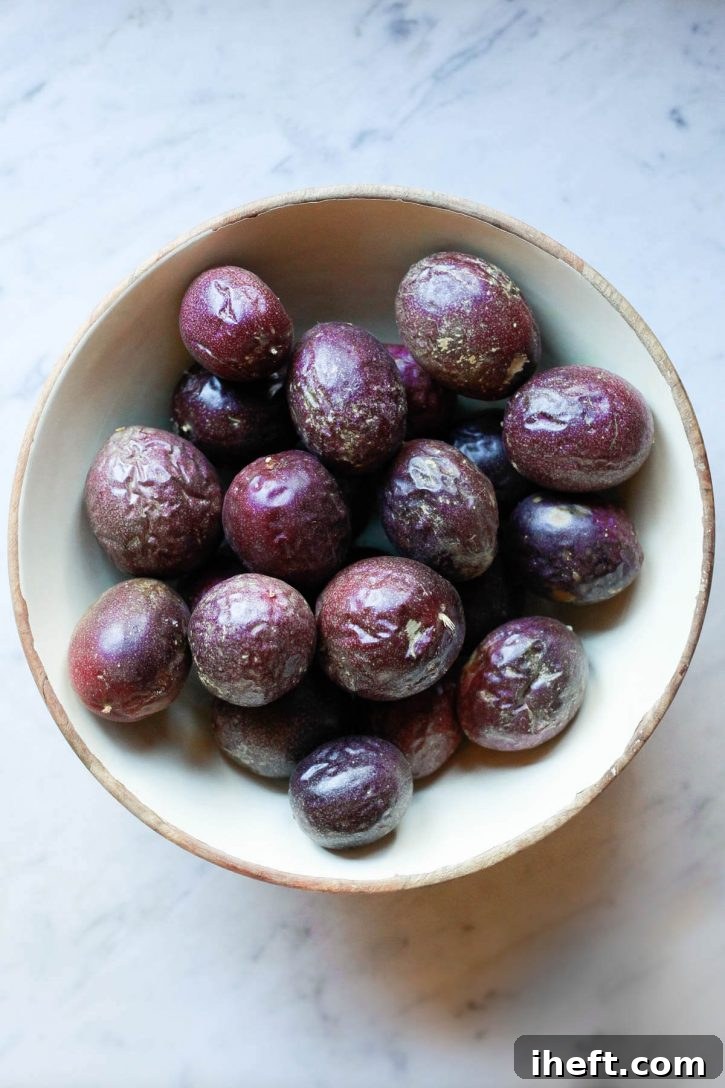 A large ceramic bowl brimming with wrinkled, ripe purple passion fruit, resting on a polished marble surface.