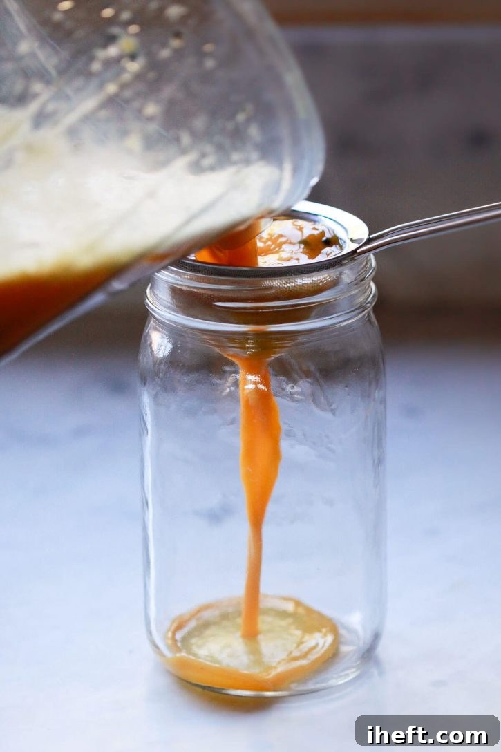 Freshly blended passion fruit juice is poured through a fine mesh sieve into a clear glass jar, separating the juice from the seeds.