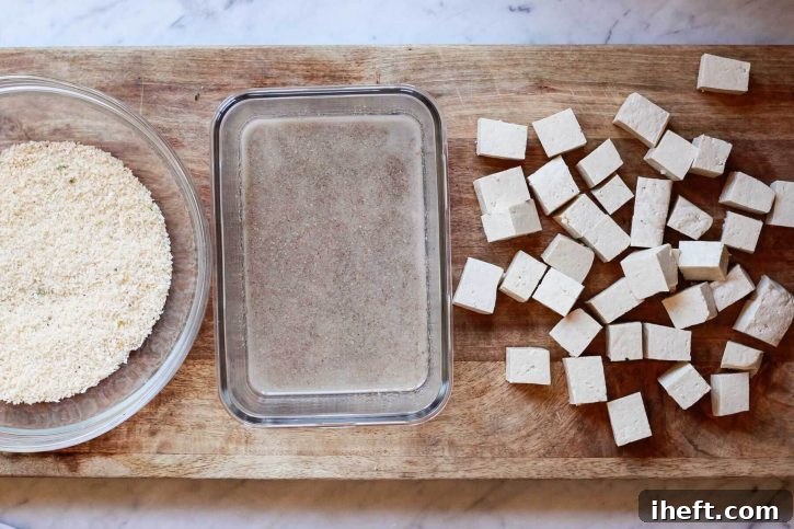 A dish of panko breadcrumbs, another dish of flax egg coating, and tofu cubes on a work surface.
