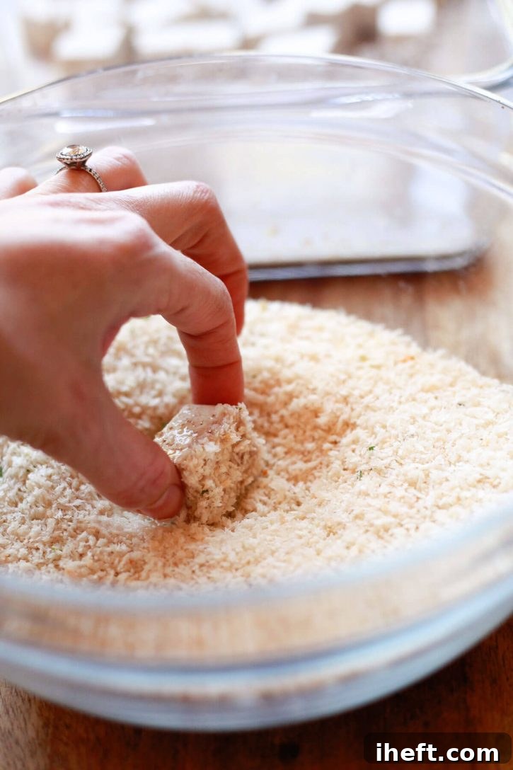 A cube of tofu is rolled in panko breadcrumbs while making crispy baked tofu nuggets.