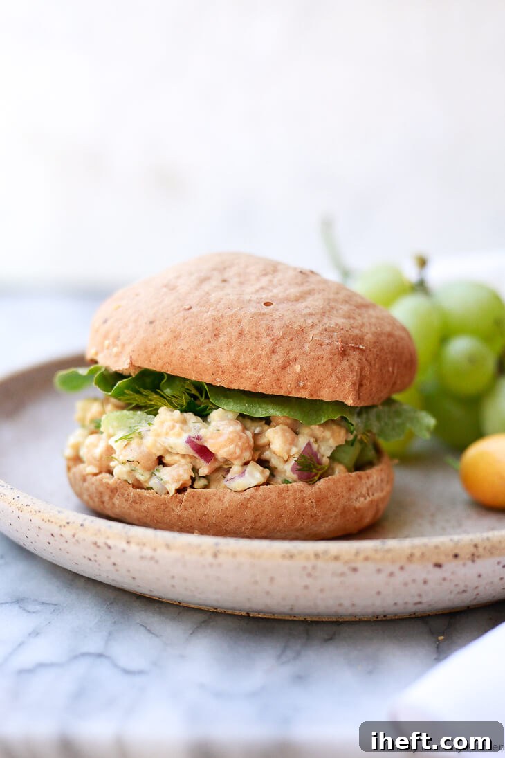 A hearty chickpea salad sandwich on toasted bread, garnished with fresh greens.