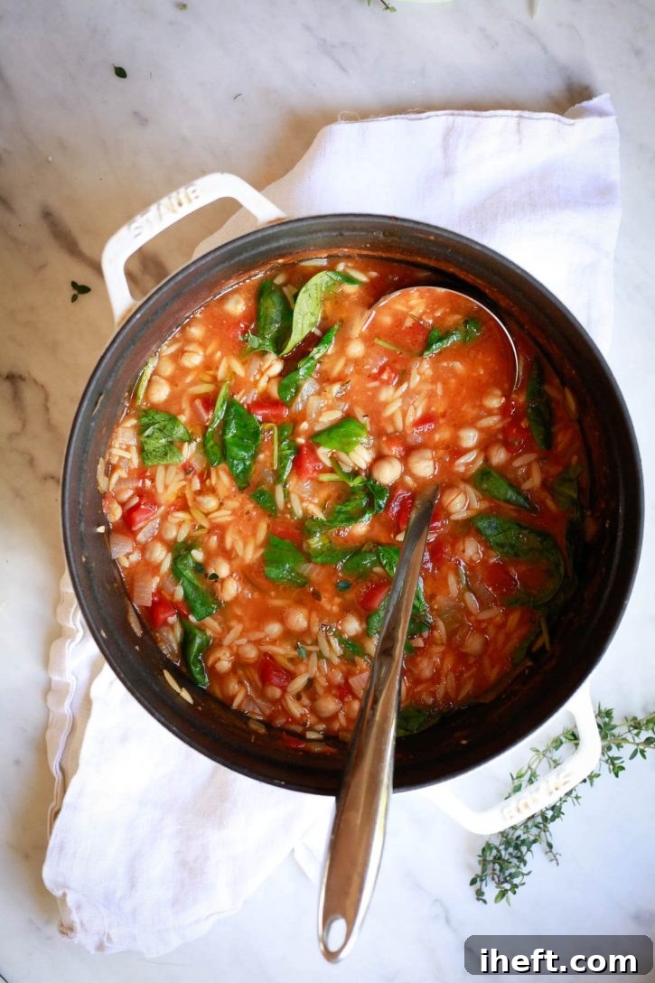 A white Staub pot filled with pasta e ceci Italian chickpea tomato soup with orzo pasta and spinach. 
