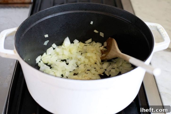 Onions are sauteed in a white pot on the stove to begin making soup. 