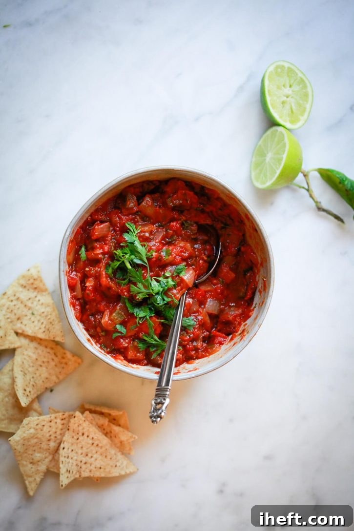 A bowl of homemade salsa roja sits on a countertop with tortilla chips. This easy homemade cooked salsa recipe is made with canned or fresh tomatoes, chipotle peppers, cilantro, and lime. 