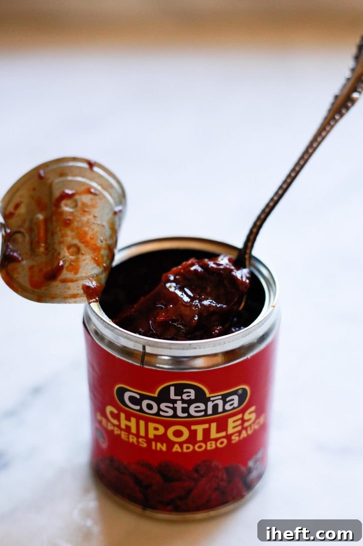 An open can of chipotles peppers in adobo sauce sits on a counter. Chipotles add heat and smoky flavor to homemade cooked salsa recipes. 