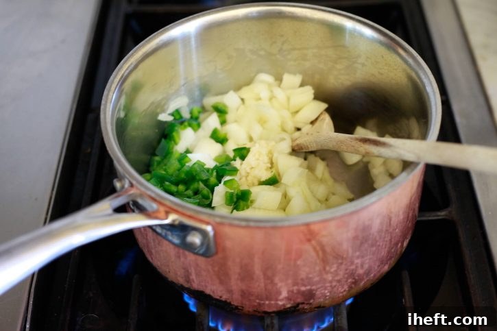 Onions, garlic, and jalapenos saute in a saucepan on the stove. 