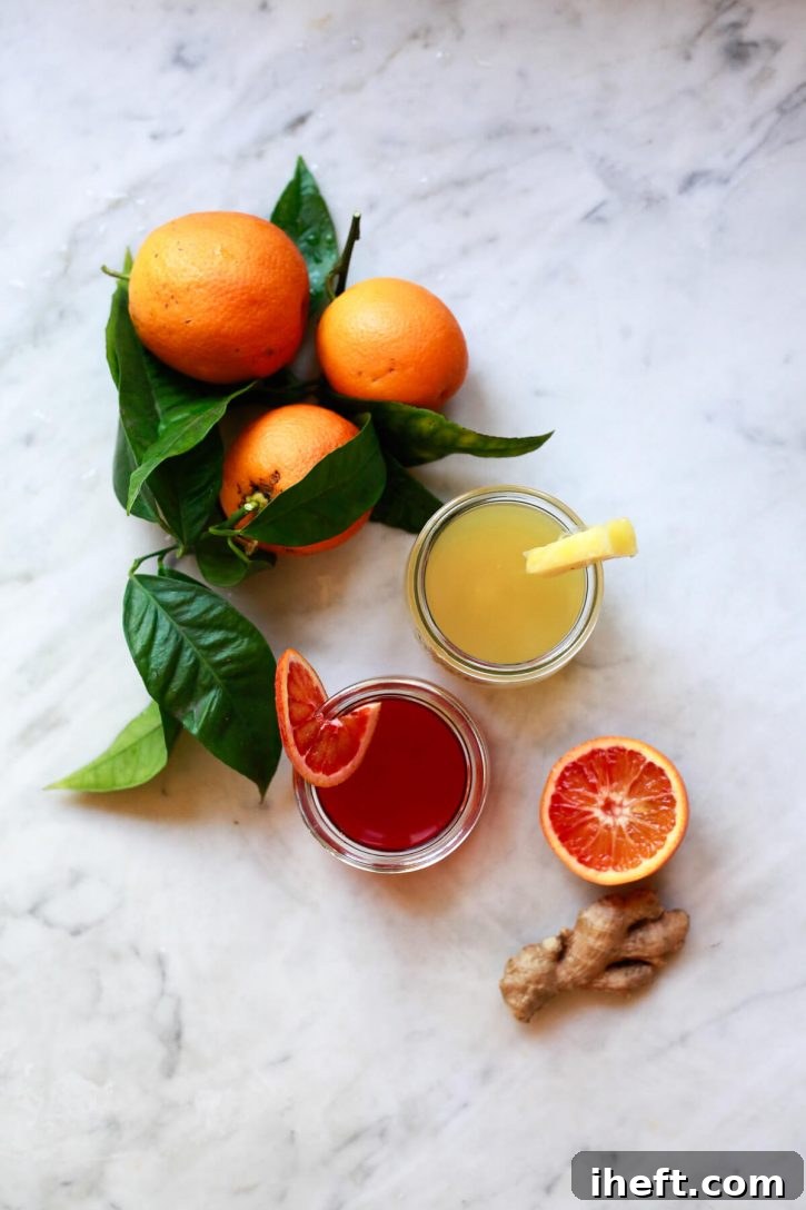 Two vibrant homemade apple cider vinegar shots, one orange-hued and one pineapple-yellow, nestled in small glass Weck jars on a pristine kitchen counter. Freshly picked oranges and robust ginger roots are artfully arranged nearby, highlighting the natural ingredients used in these wellness beverages.