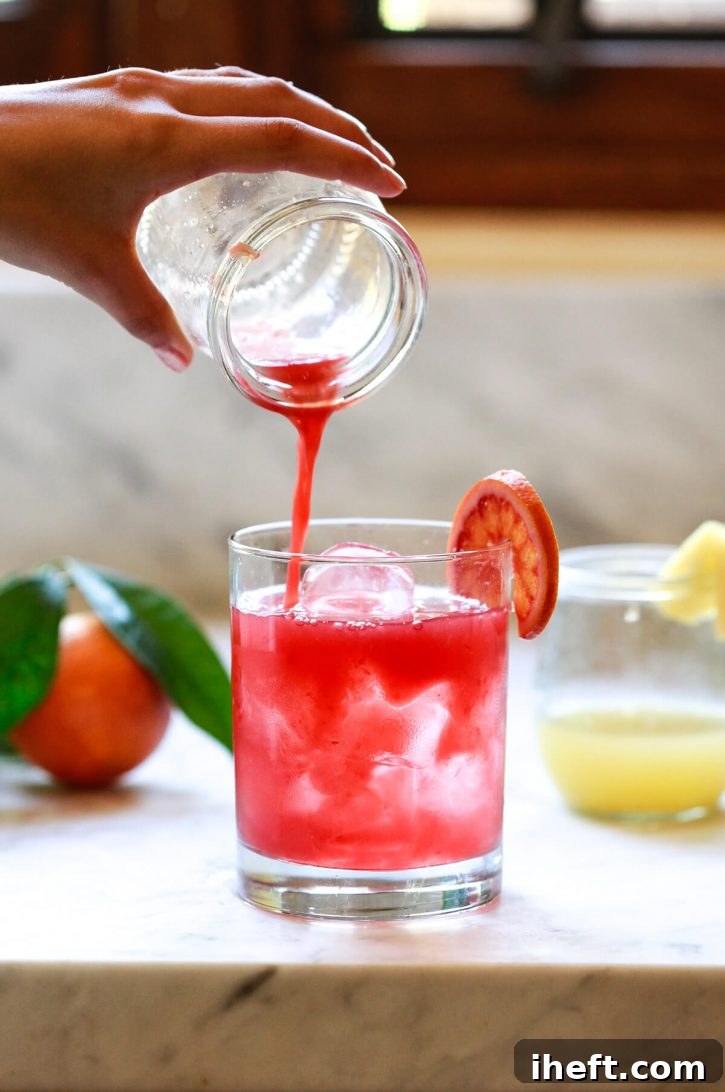 A small, prepared apple cider vinegar shot, vibrant with juice and ginger, is carefully poured into a tall glass filled with refreshing ice water. This visual emphasizes the crucial step of diluting ACV shots before consumption for safety and palatability.