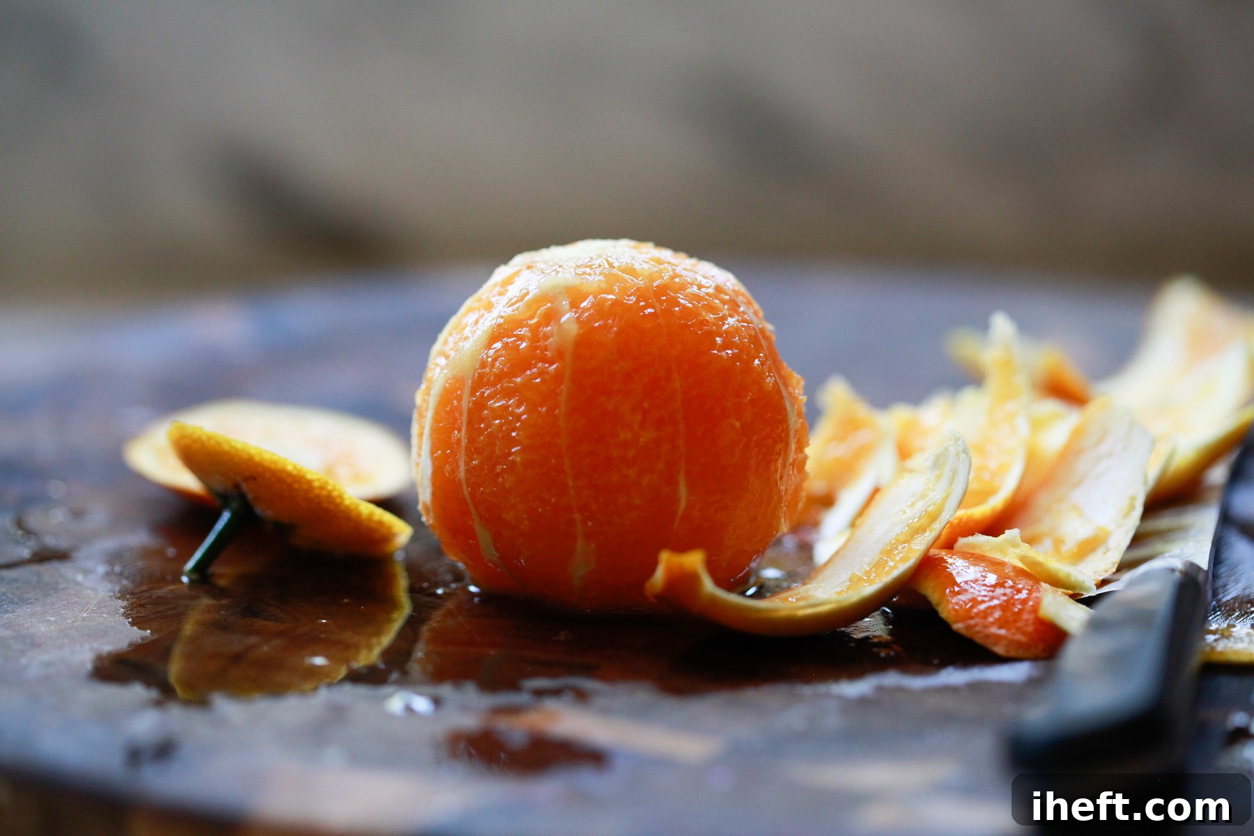 A peeled orange sits on a cutting board, ready for slicing. The white pith has been completely removed, revealing the bright orange flesh.