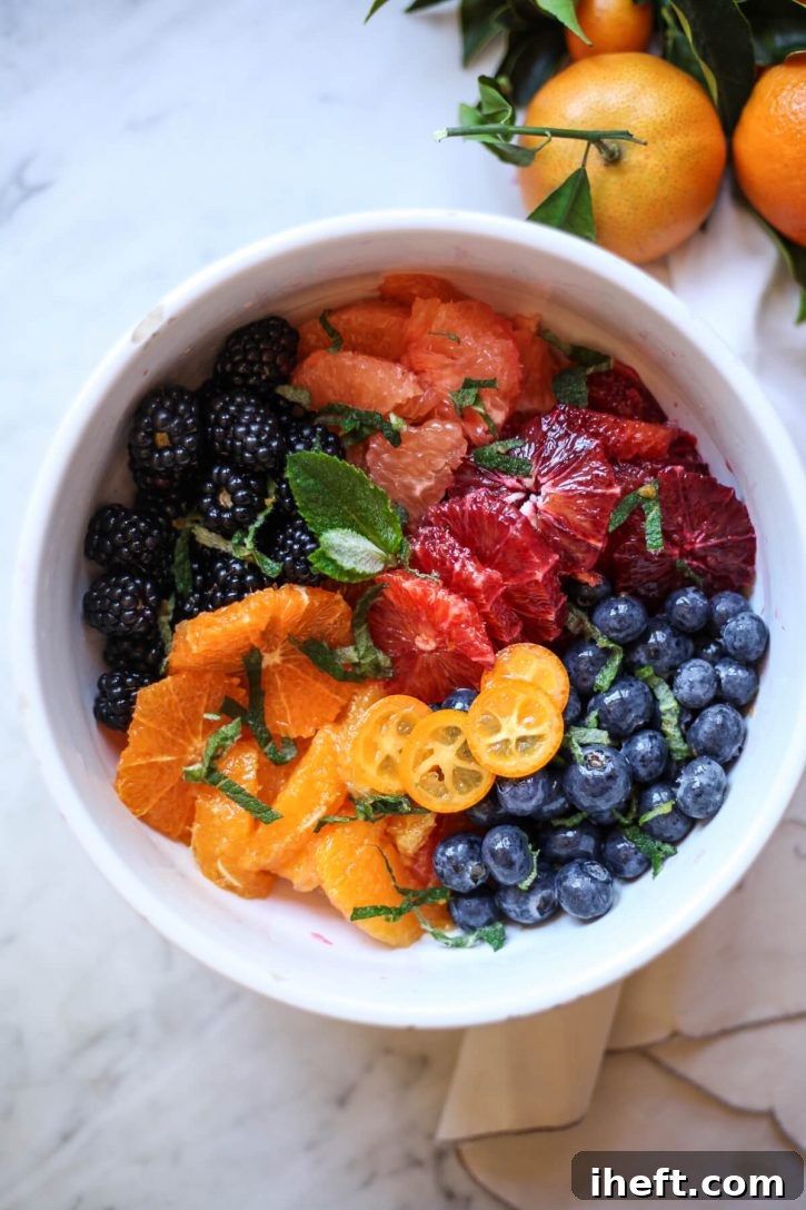 A round bowl filled with a homemade citrus fruit salad, featuring juicy blood oranges, sweet oranges, plump blueberries, rich blackberries, and fresh mint leaves, creating a refreshing spring dessert.