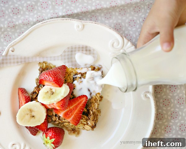 A child's hand pours milk over a plate of baked oatmeal with nutella, bananas, and strawberries.