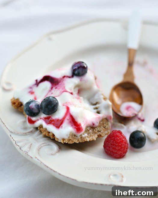 A perfectly sliced portion of the Red, White, and Blue Ice Cream Pie, revealing its distinct layers of creamy ice cream, vibrant berry swirls, and crunchy granola crust, garnished with fresh berries.