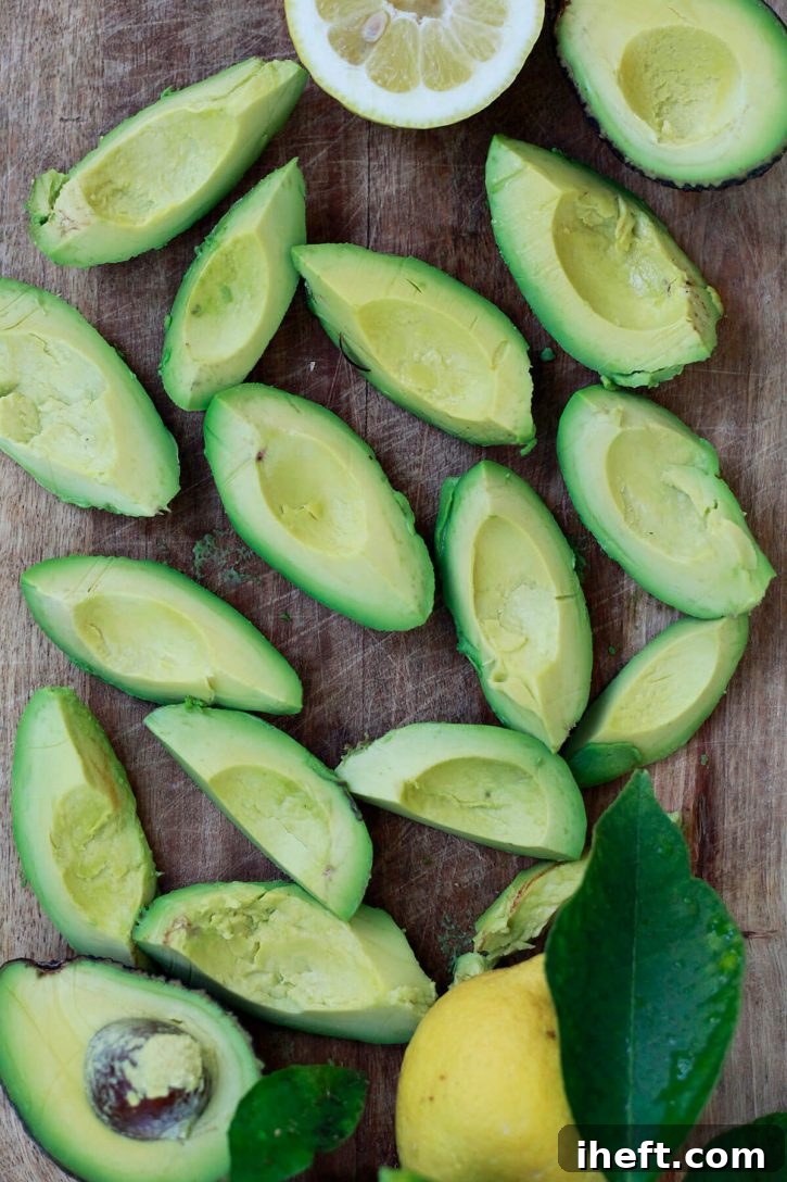 Freshly peeled avocado quarters neatly laid out on a cutting board, prepared and ready for the freezing process.