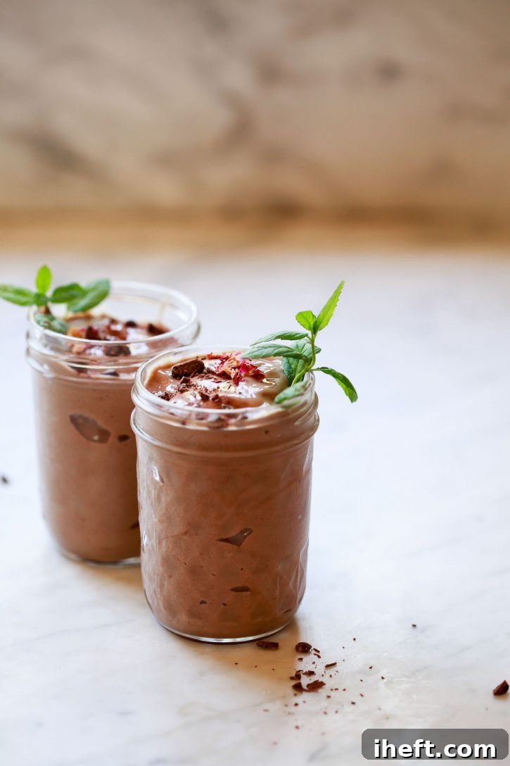 Two chocolate avocado smoothies garnished with mint and dark chocolate sit on a marble kitchen countertop. 