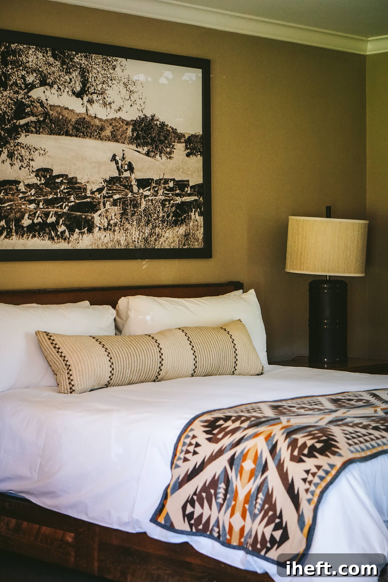 A luxury dude ranch Western themed bedroom at Alisal Ranch. A bed with white linens and a vintage photograph above the bed of Alisal cattle and cowboys. 