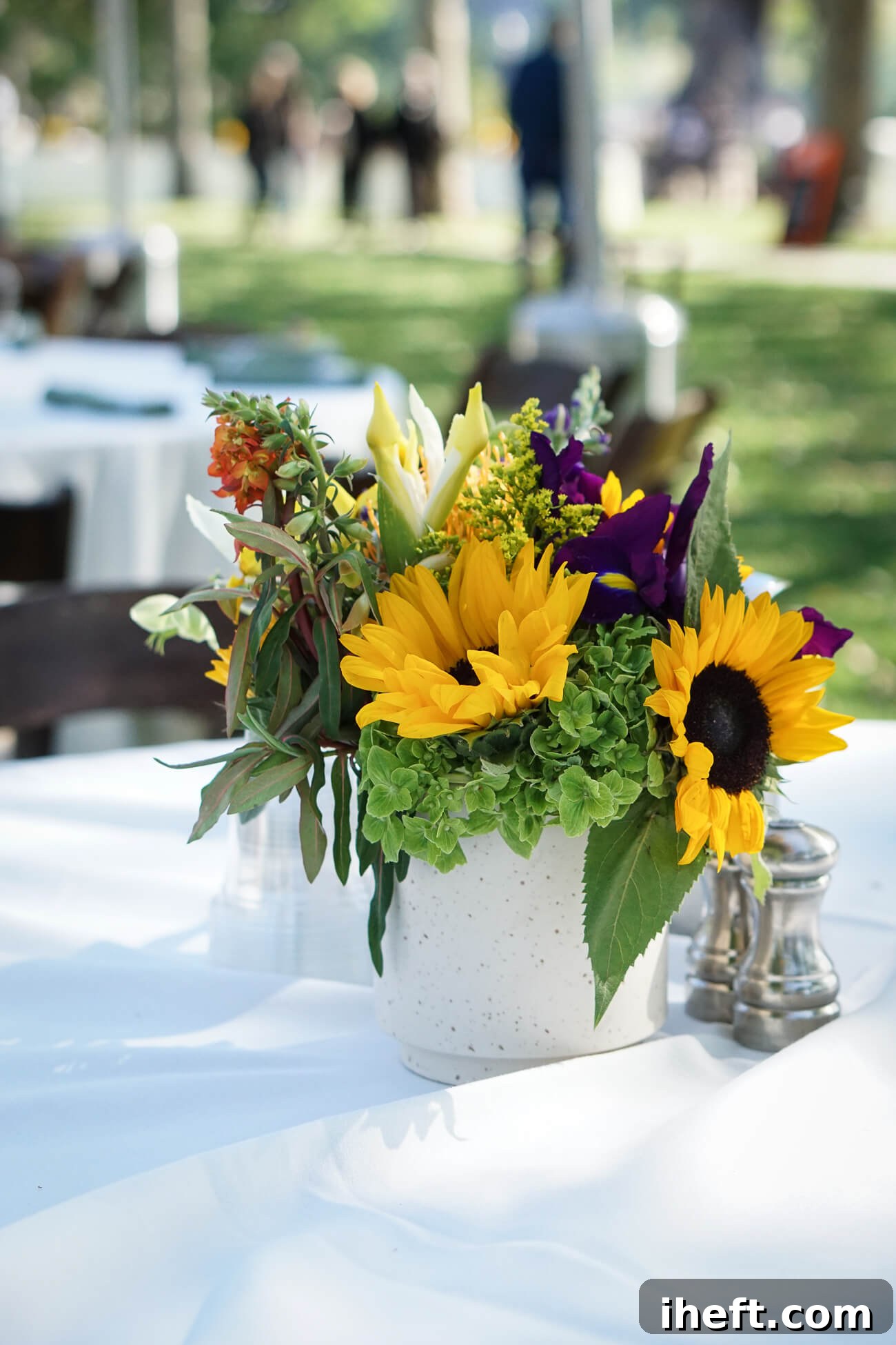 A floral arrangement with sunflowers, green hydrangea and other flowers on an outdoor dining table. 