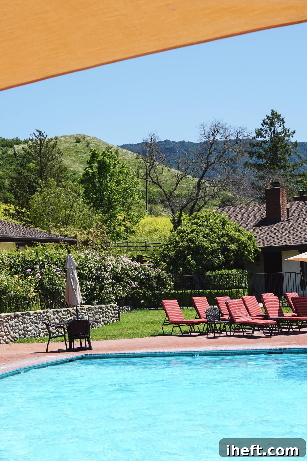 A light blue pool with rust-colored lounge chars and green hills in the background. A corner of the pool at Alisal Ranch. 