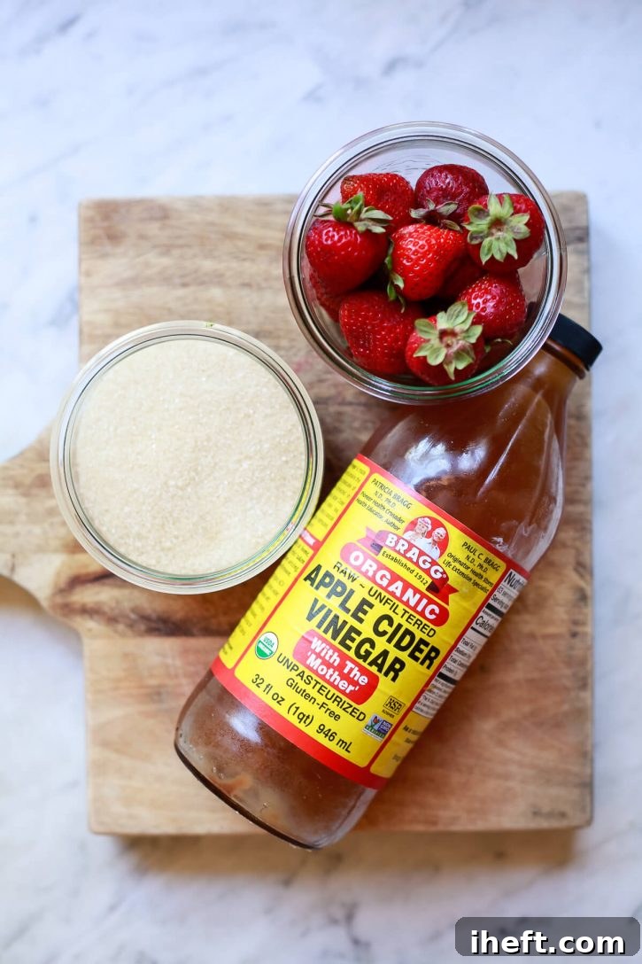 A bottle of Bragg's apple cider vinegar, fresh strawberries, and sugar sit on a counter to illustrate how to make a shrub drink. 