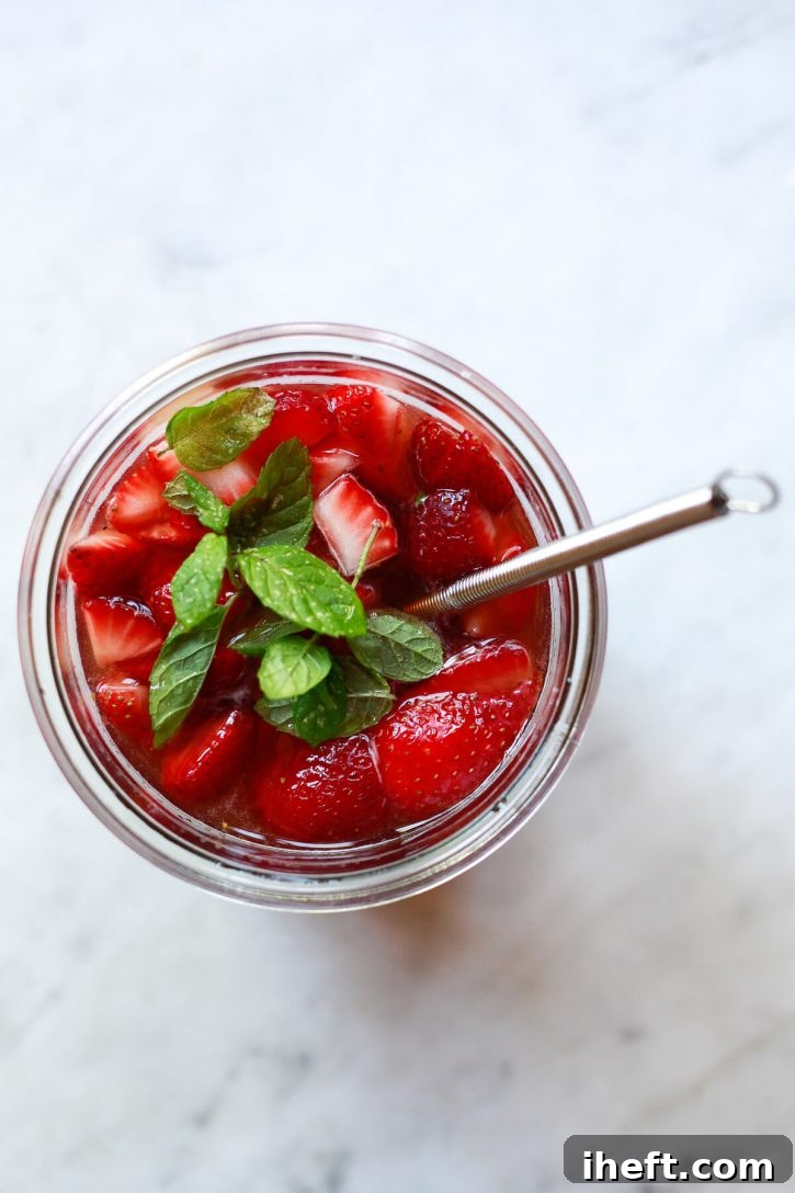 An overhead photo of how to make a shrub drink. Fresh strawberries, mint, and vinegar are whisked together in a jar. 
