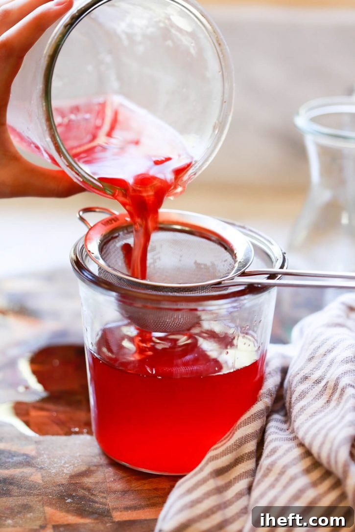 Bright red strawberry drinking vinegar (shrub syrup) is poured through a fine mesh sieve to strain strawberries. 
