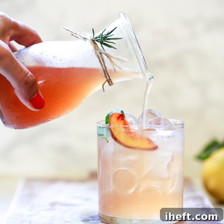 A bottle of a peach shrub drink pours into a glass of ice and water.