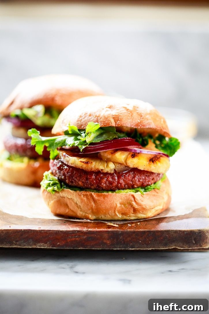 Hamburgers topped with grilled pineapple, teriyaki sauce, onion, avocado and lettuce sit on a cutting board. Delicious looking juicy vegan pineapple burgers.