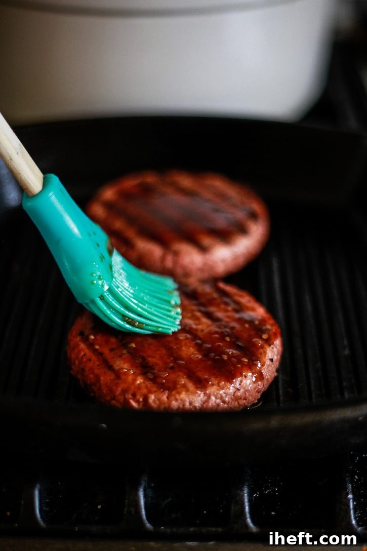 Two plant-based vegan hamburger patties grill on a grill pan while being brushed with teriyaki sauce to make pineapple teriyaki veggie burgers.