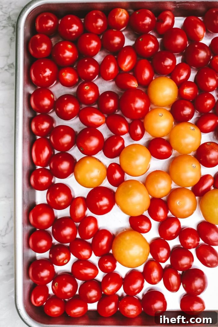 Whole fresh cherry tomatoes sit on a sheet pan before going into the freezer. This is the essential first step in how to freeze cherry tomatoes and other small varieties.