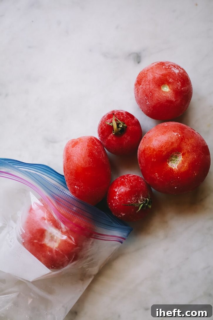 Frozen whole tomatoes coming out of a ziplock bag, ready for long-term storage or immediate use.