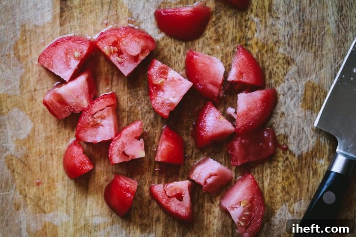 Roma tomatoes that have been frozen, thawed, peeled, and neatly chopped on a cutting board, demonstrating their readiness for cooking.