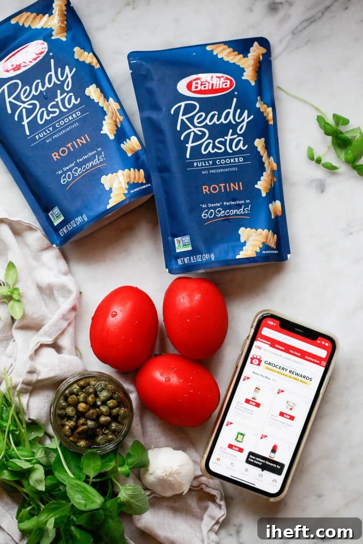 Two vibrant blue packages of Barilla Ready Pasta Rotini are neatly arranged on a kitchen countertop alongside a selection of fresh, colorful ingredients: ripe Roma tomatoes, fragrant fresh basil, cloves of garlic, and a small jar of briny capers. This inviting display highlights all the components needed for a quick and delicious tomato basil pasta.