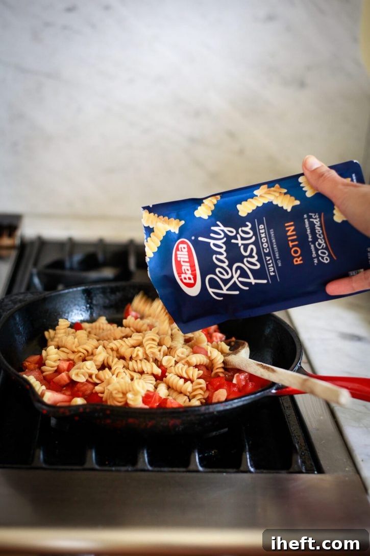 Perfectly cooked Barilla Ready Pasta Rotini is introduced into a bustling skillet, joining the vibrant mixture of softened tomatoes, fragrant garlic, and capers, all being tossed together to create a quick and easy tomato basil pasta recipe.
