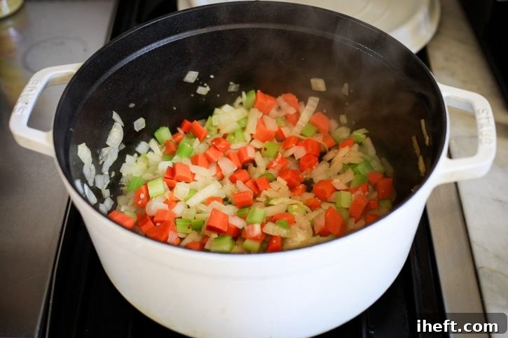 Diced onions, carrots, and celery gently sautéing in a white enameled pot, forming the aromatic 'soffritto' foundation for an authentic Ribollita.