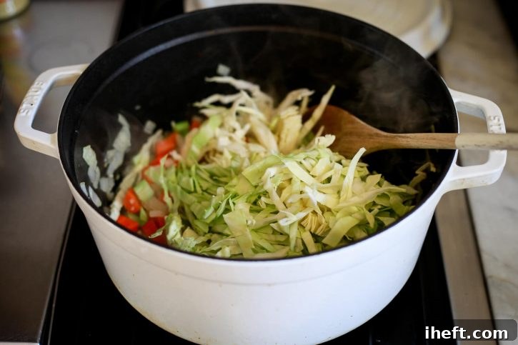 Freshly shredded green cabbage being added to a large pot, beginning the layering process for a rich and flavorful Ribollita soup.