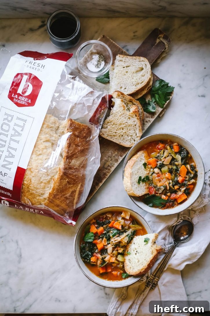 Two enticing bowls of hearty Tuscan Ribollita soup artfully presented on a sleek marble countertop, accompanied by slices of rustic La Brea Italian Round bread. This wholesome Tuscan bread, vegetable, kale, and white bean soup stands as a healthy and utterly delicious vegetarian and vegan comfort food meal.