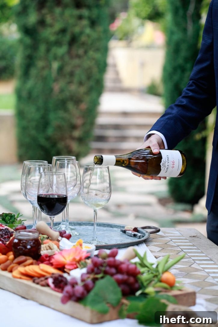 A man gracefully pours a glass of crisp Noble Vines Chardonnay into a wine glass at a relaxed backyard home wine tasting party, set against the warm glow of evening lights.