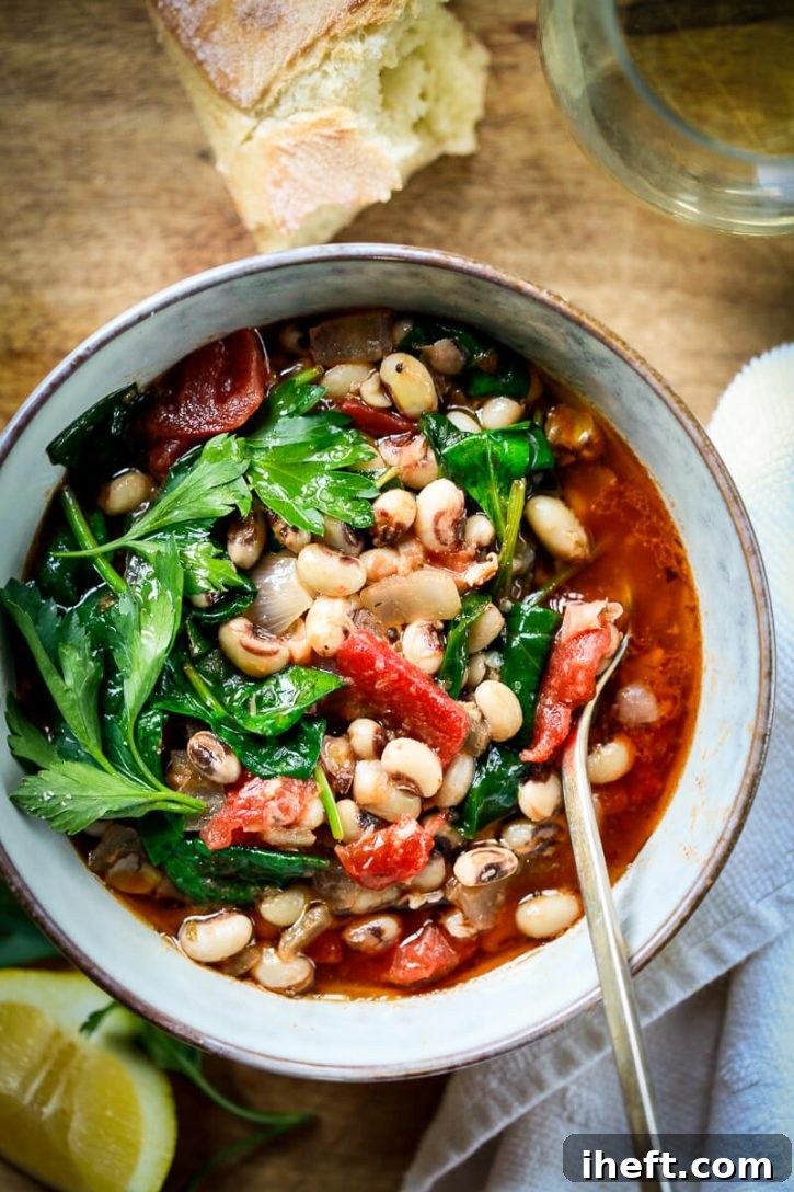 A vibrant bowl of healthy vegan stewed black eyed peas, rich with tomatoes, broth, fresh spinach, and a zesty lemon wedge. 