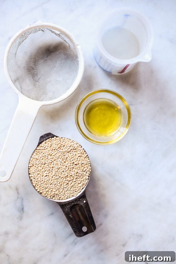 A small measuring cup of dry quinoa, a tablespoon of olive oil, a glass of water, and a fine mesh sieve are neatly arranged on a pristine marble countertop, ready for cooking quinoa in the Instant Pot.