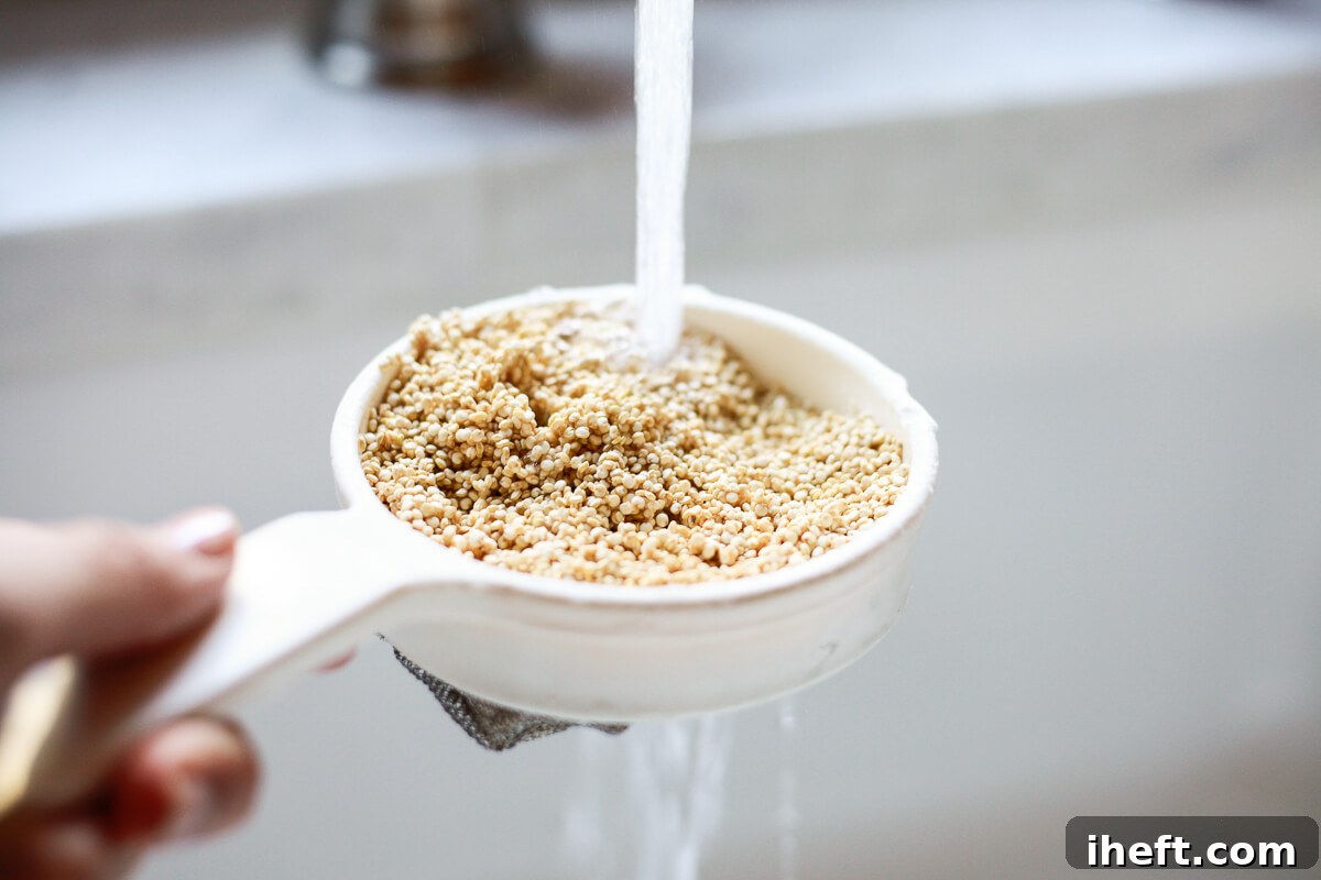 Quinoa being rinsed in a fine mesh sieve under a kitchen faucet.
